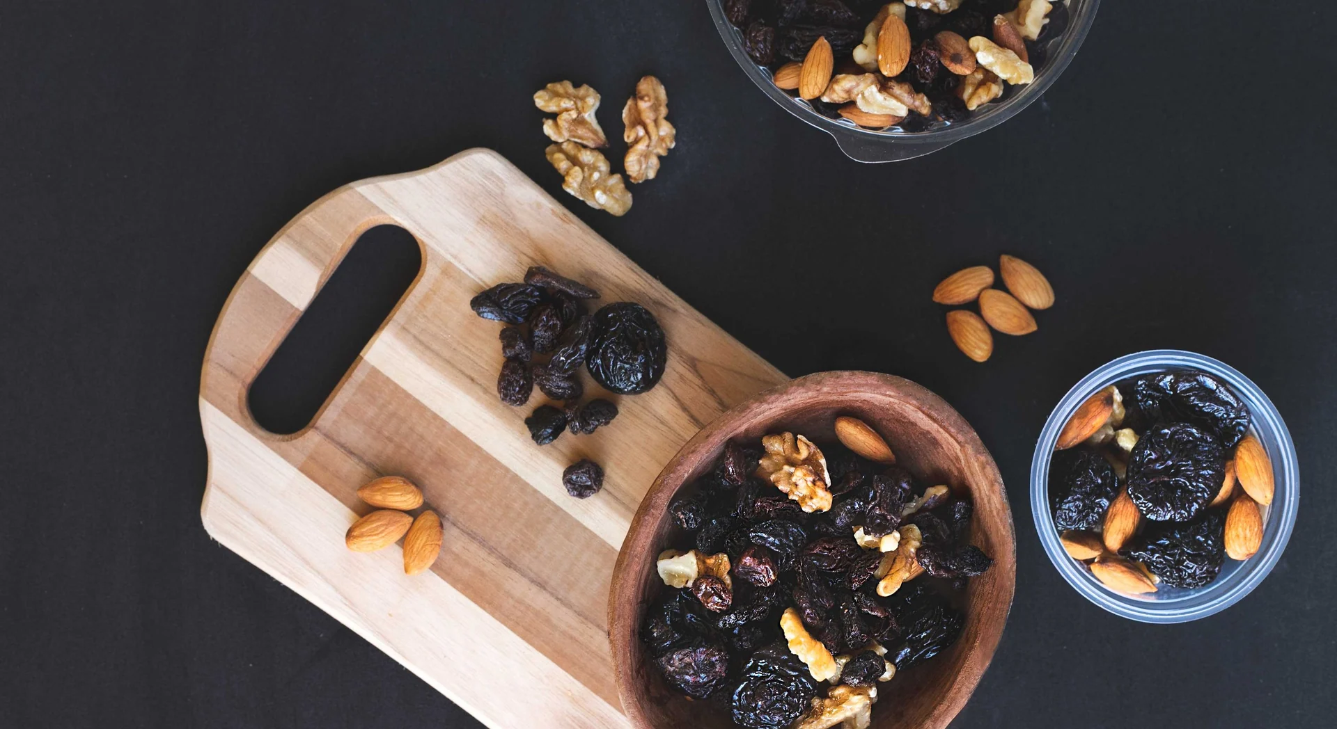 Almonds, walnuts and dried fruits arranged in bowls on a dark table